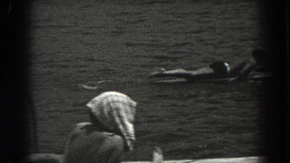 1938 New Jersey home-movie frame showing a dock edge, rippling water, and a person floating on a board beyond a foreground figure.