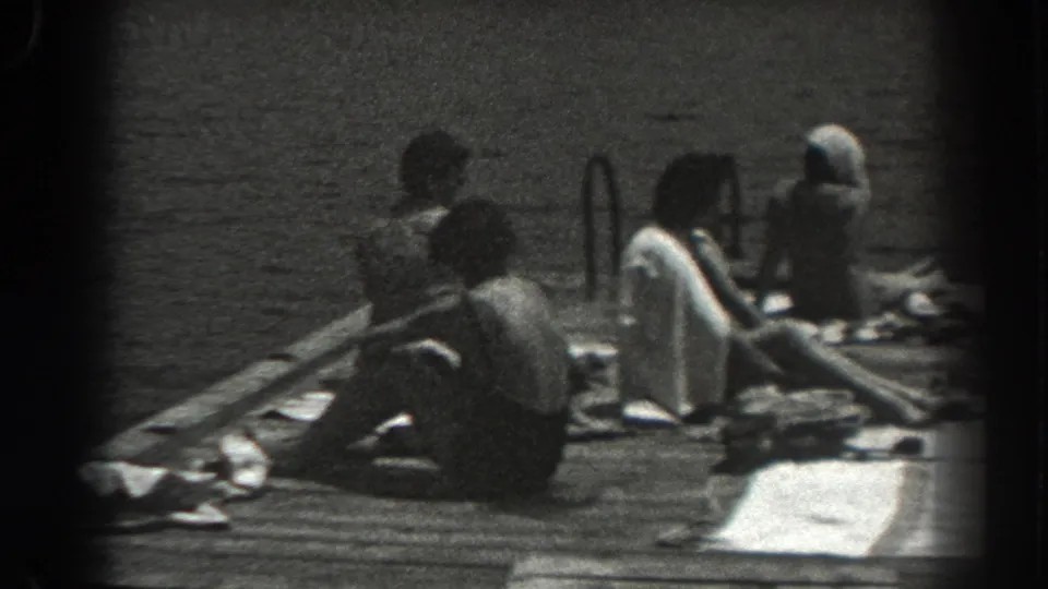 1938 New Jersey dock scene with seated sunbathers in swimwear, towels on the planks, water behind them, and a metal ladder at the edge.