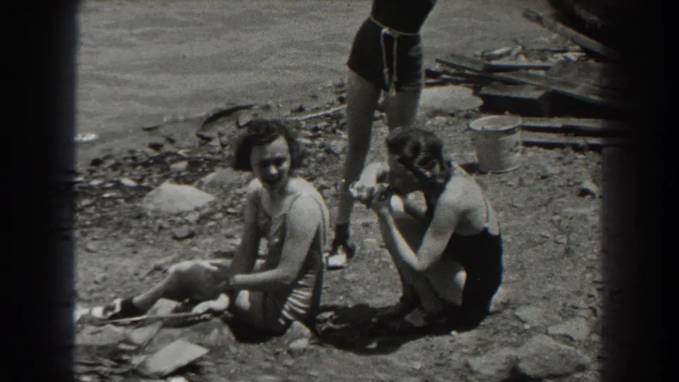 1938 New Jersey home-movie still of women in swimsuits on a sunlit rocky lakeshore, with one figure partly cropped by the frame.