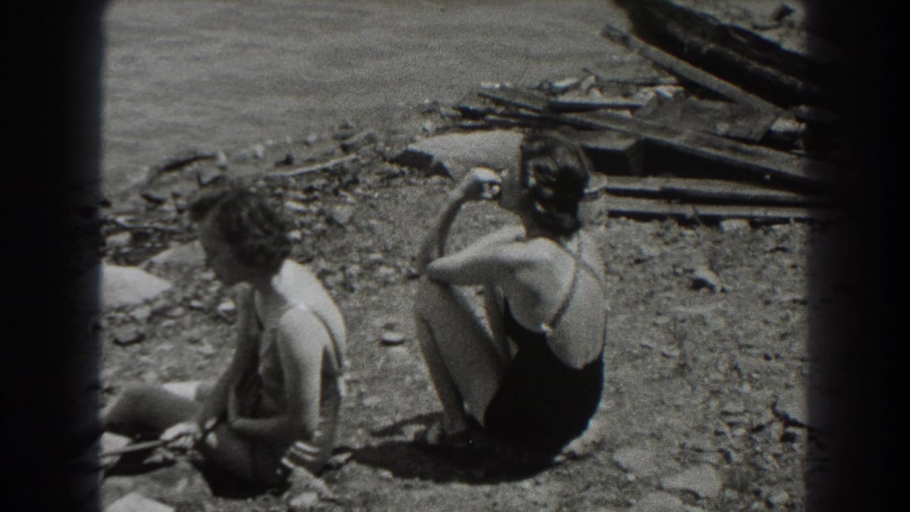 Two adult women in swimsuits sit on a rocky New Jersey shoreline in 1938 home-movie footage, one turned away and one nearer the camera.