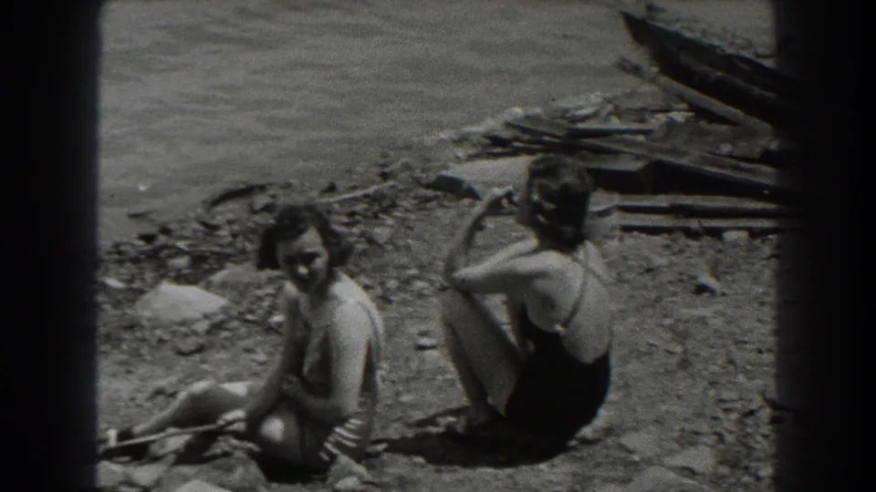 In 1938 New Jersey, two women in period swimwear sit near lake water while one in a dark suit holds a cigarette.