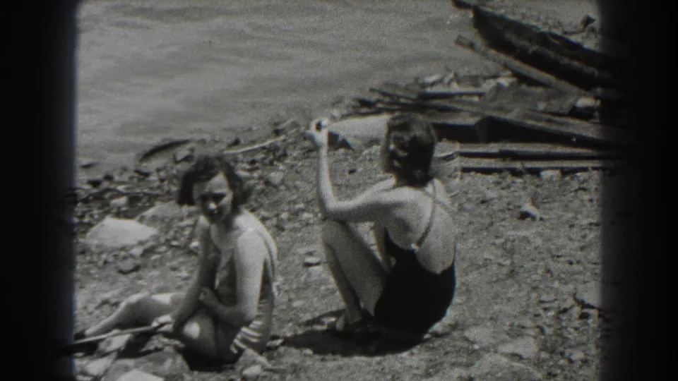 Two women in swimsuits sit on a New Jersey lakeshore in 1938, one facing the camera and the other turned partly away while smoking.