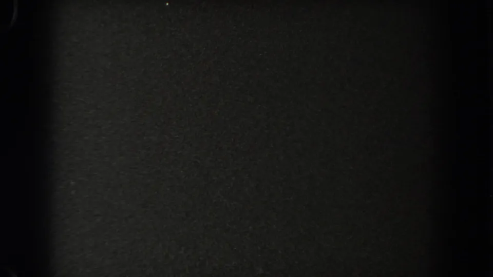 A nearly black 8mm frame shows film grain and minimal detail, suggesting the clip has moved into a reel transition or exposure change.