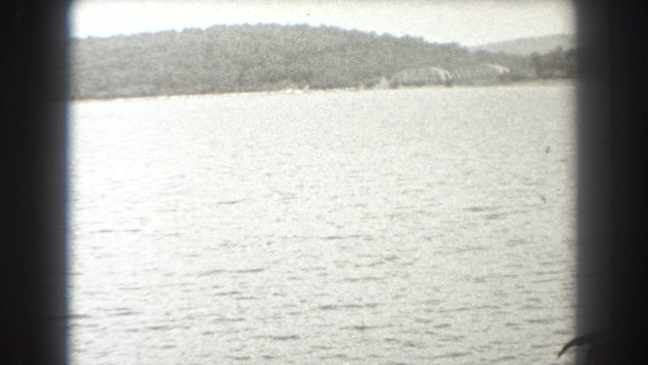 1938 New Jersey 8mm frame showing bright open water, distant wooded land, and dark framing that suggests a boat window or film gate.