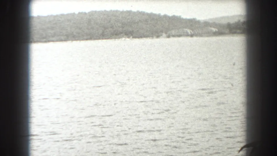 1938 New Jersey 8mm frame showing bright open water, distant wooded land, and dark framing that suggests a boat window or film gate.