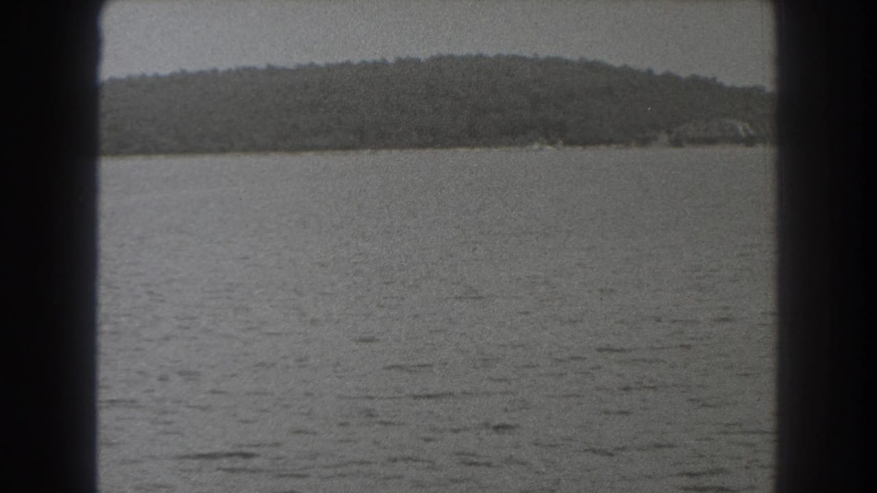 1938 New Jersey home-movie frame with muted water, a low wooded shoreline, gray sky, and heavy dark framing at the sides.