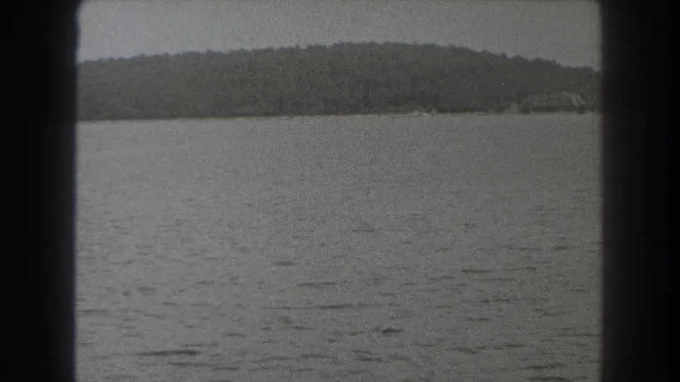 1938 New Jersey home-movie frame with muted water, a low wooded shoreline, gray sky, and heavy dark framing at the sides.