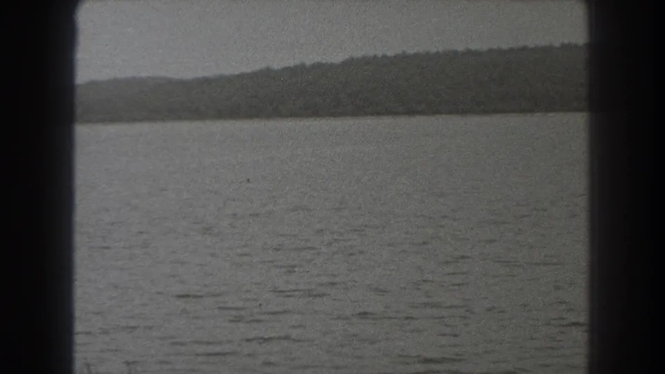 Late-clip 1938 New Jersey frame showing calm rippled water, a distant dark shoreline, and the soft grain of scanned 8mm film.