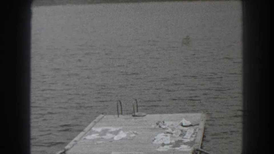 1938 New Jersey lakeside frame showing a concrete dock, metal ladder rails, lake water, and distant shoreline.