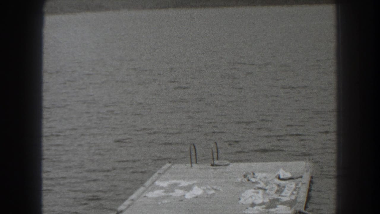 Calm lake water seen past a dark frame with a small dock or platform at lower left.