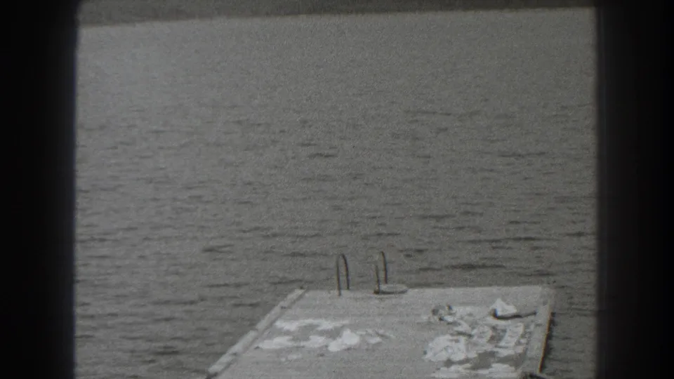 1938 New Jersey 8mm frame showing calm lake water, a distant shore, and a small dock or platform partly framed by dark edges.