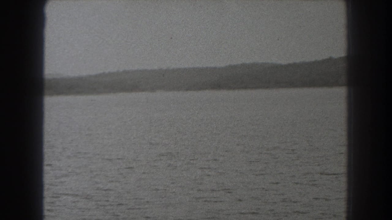 1938 New Jersey 8mm frame looking over rippled lake water toward a low wooded ridge, bordered by a dark vertical edge.