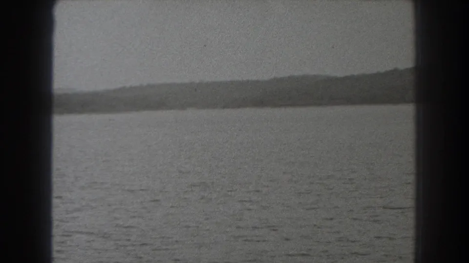 1938 New Jersey 8mm frame looking over rippled lake water toward a low wooded ridge, bordered by a dark vertical edge.