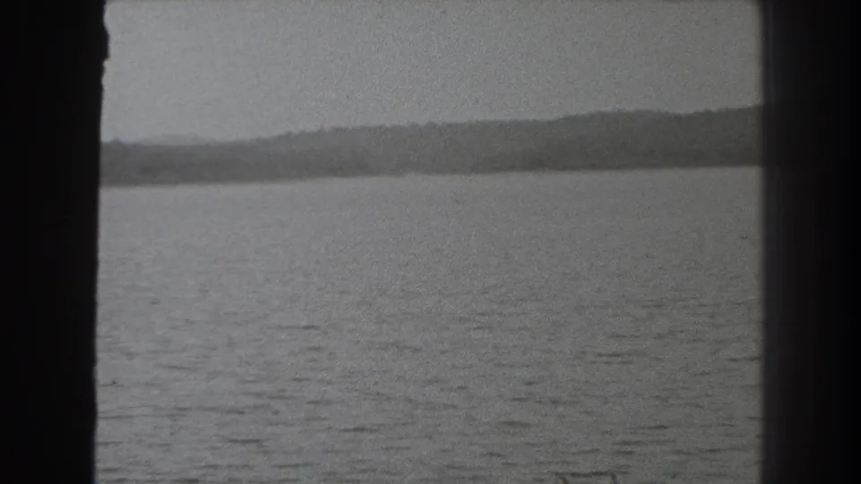 1938 New Jersey 8mm frame with calm water, distant hills, and dark side framing suggesting a window or boat structure.