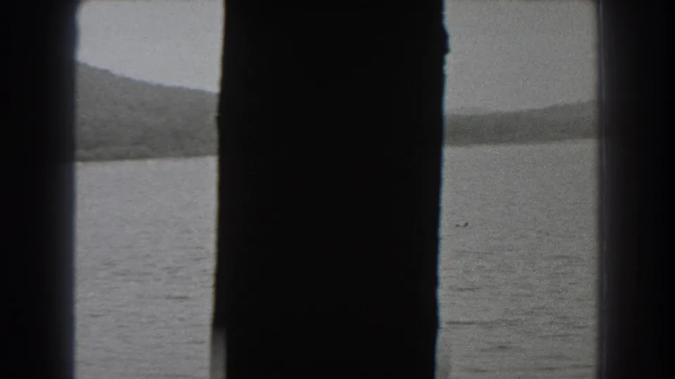 1938 New Jersey 8mm frame showing open lake water and a low hillside, partly blocked by a dark vertical structural edge.