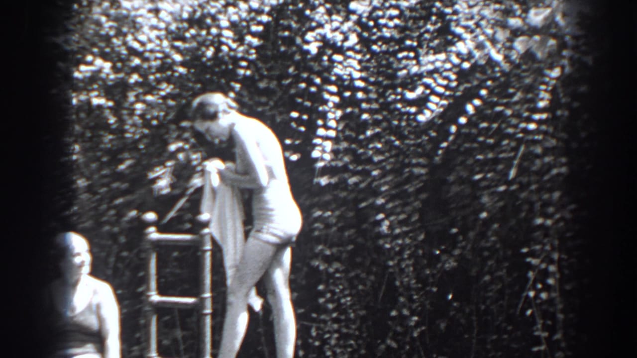 Two women in swimwear near a metal ladder in front of a leafy hedge.