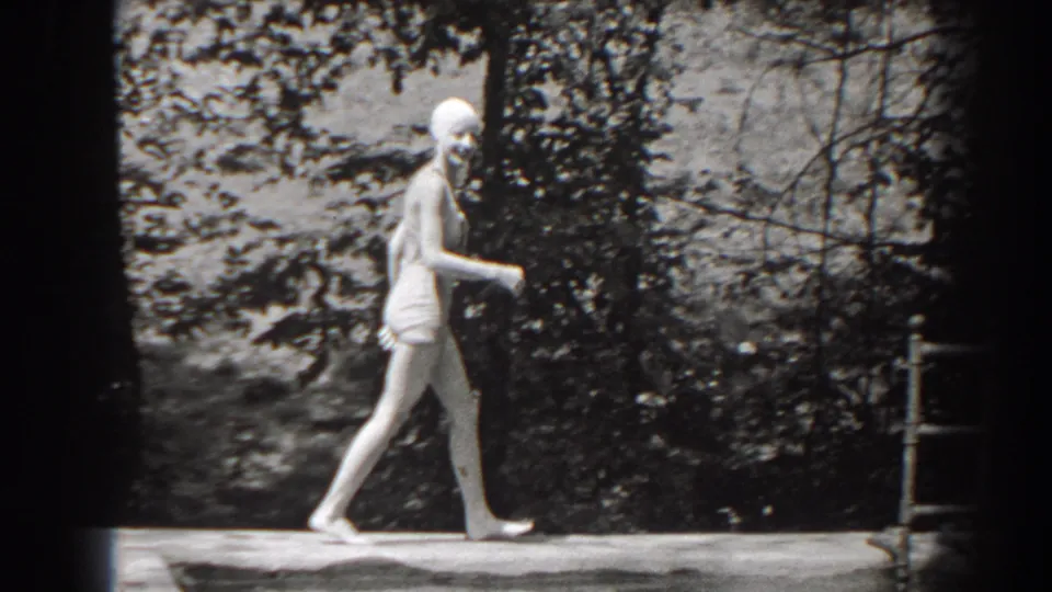 In 1938 New Jersey home-movie footage, a young woman in a swim cap and one-piece swimsuit walks along a tree-lined pool edge.