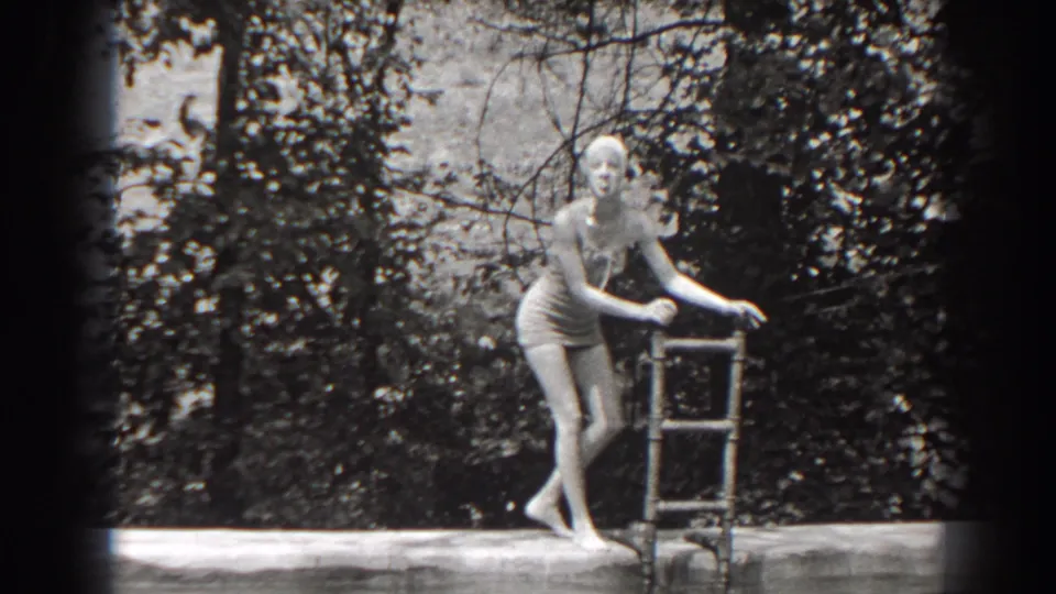 The swimmer reaches the metal pool ladder, with trees and shrubs behind her in the 1938 New Jersey outdoor scene.