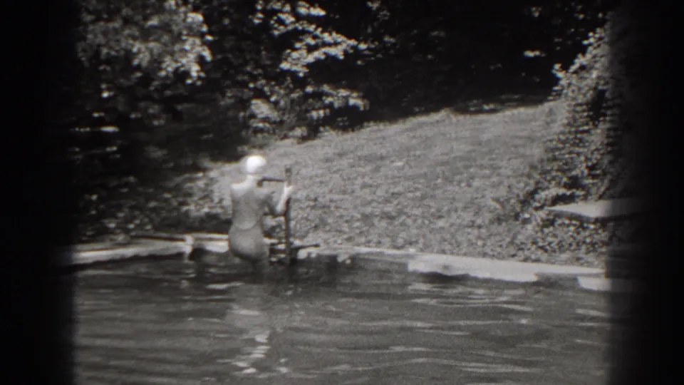 The woman descends the ladder into the pool, partly turned away, with water, lawn, and trees visible behind her.