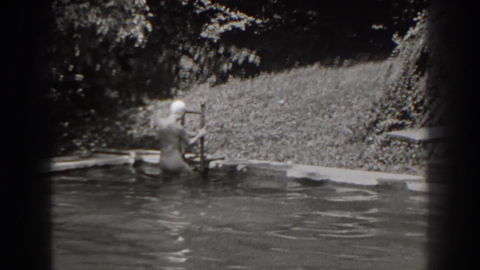 At the end of the clip, the swimmer is low on the ladder near the water, with the pool surface and grassy background visible.