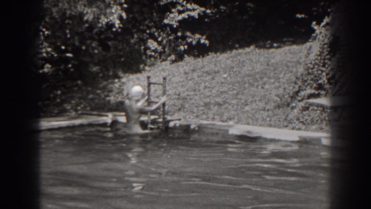 Woman in swim cap near a pool ladder beside a planted backyard edge.
