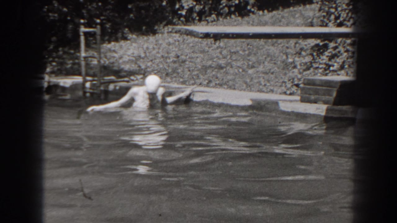 1938 New Jersey frame of a woman in a swim cap standing in pool water with a lawn, plants, and poolside edge behind her.