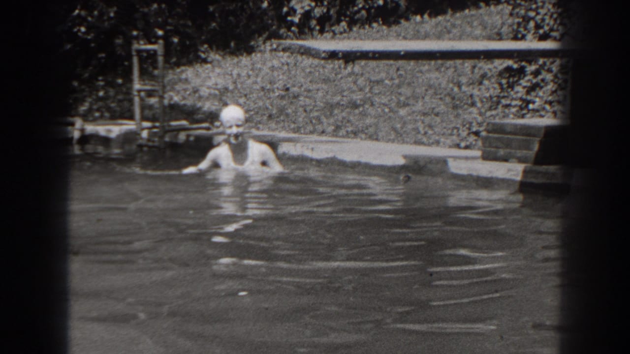 1938 New Jersey home-movie still showing the swimmer chest-deep in the backyard pool, with ladder, lawn, and plants visible.