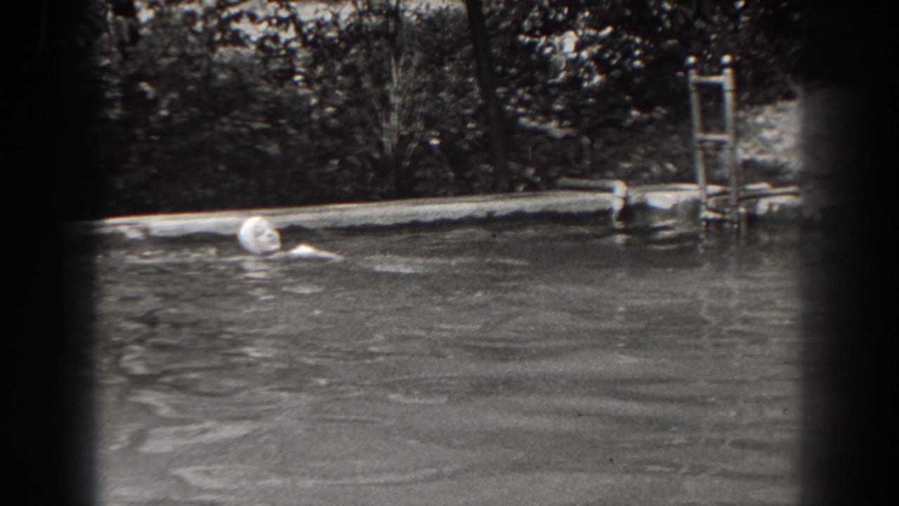 Woman in a swim cap moves through a backyard pool near a metal ladder and trees.