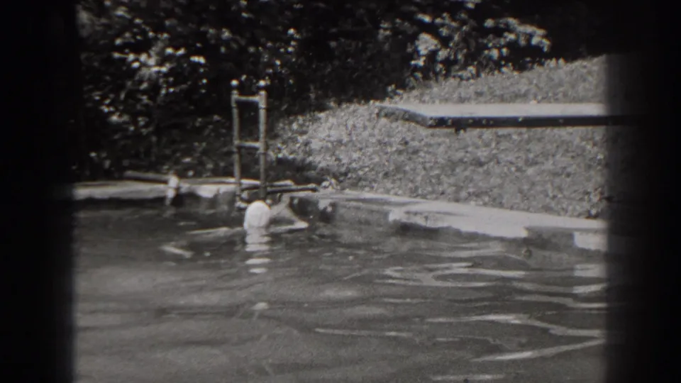 1938 New Jersey 8mm frame showing the swimmer close to the edge of the backyard pool, with ladder, water ripples, and grass behind.