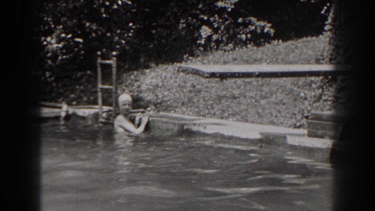 In 1938 New Jersey home-movie footage, a woman in a swim cap pauses at the edge of an outdoor pool near a ladder and diving board.