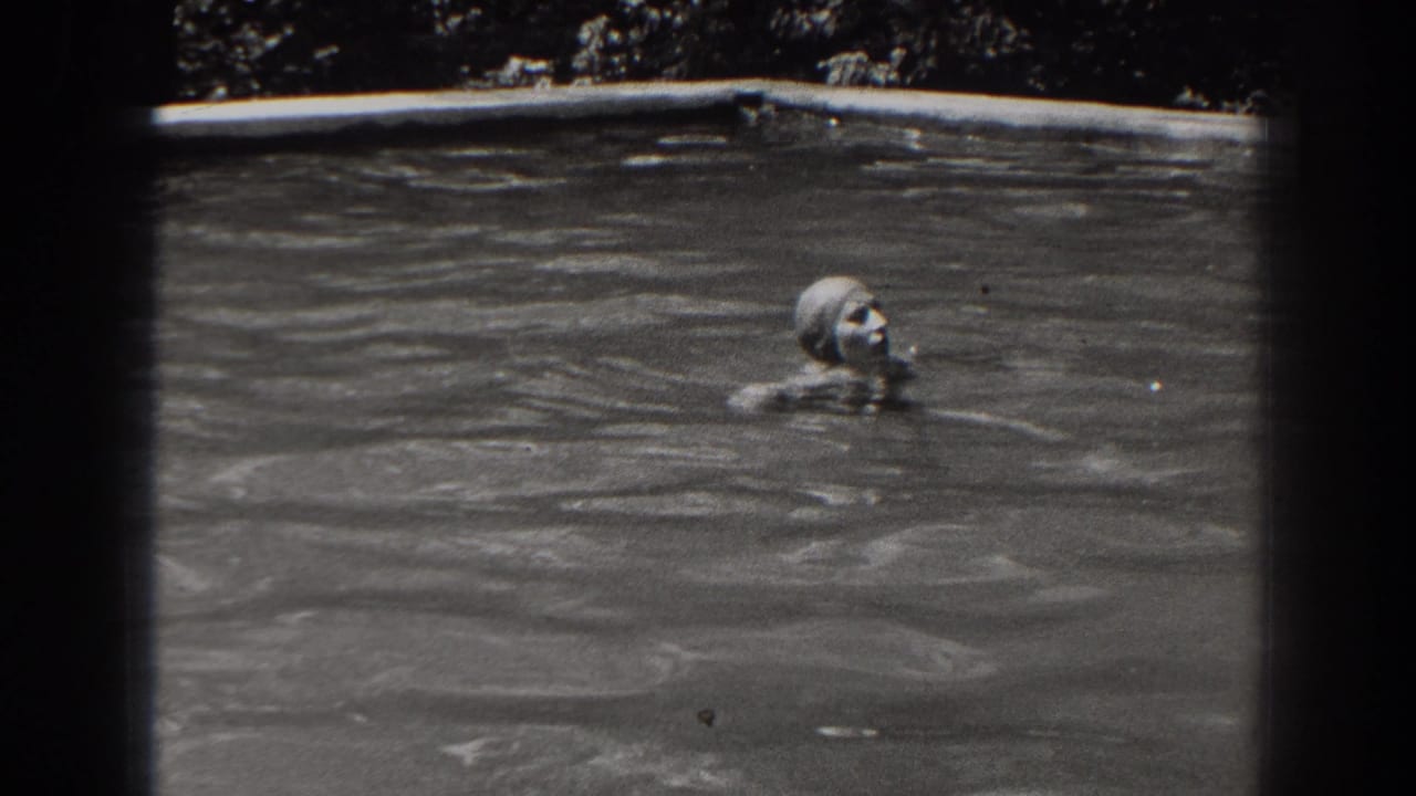 The swimmer moves through an outdoor pool in 1938 New Jersey footage, with her capped head and shoulders visible above the water.