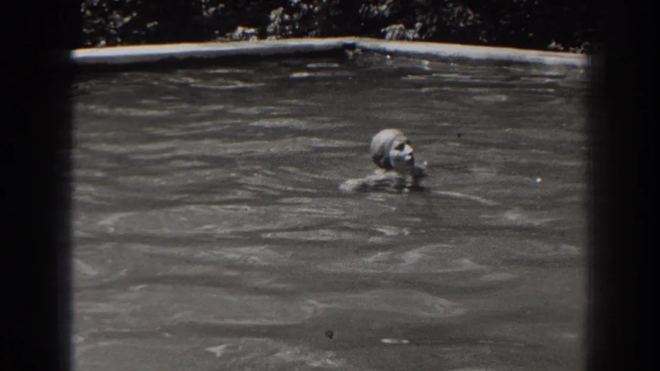 The swimmer moves through an outdoor pool in 1938 New Jersey footage, with her capped head and shoulders visible above the water.