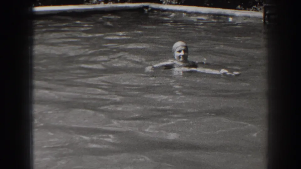 The swimmer floats with her arms extended in an outdoor pool, with rippling water and the pool edge visible behind her.