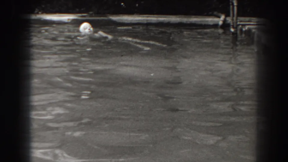 A woman in a swim cap continues swimming near the far edge of the backyard pool, with water filling most of the frame.