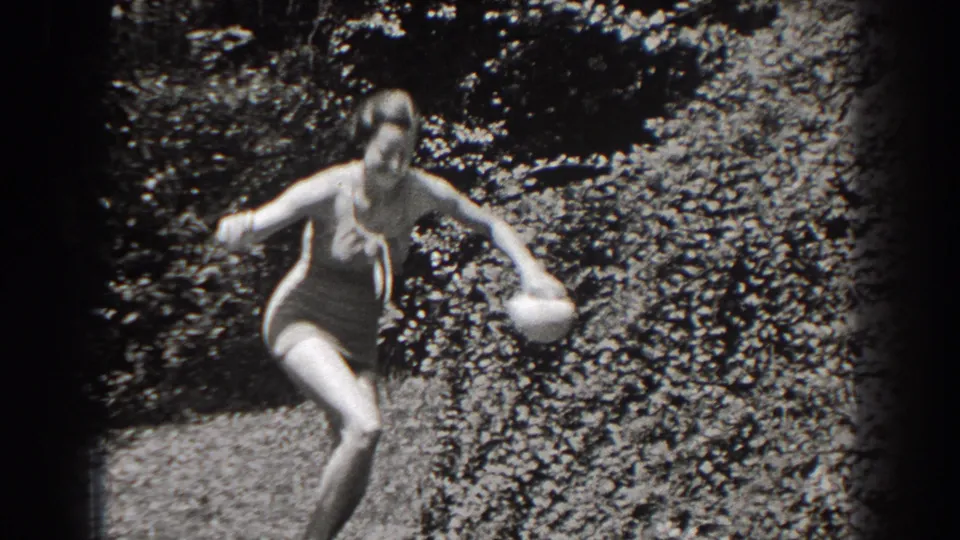 A woman in a one-piece swimsuit and swim cap moves near dense foliage at the pond or lake edge in New Jersey footage from 1938.