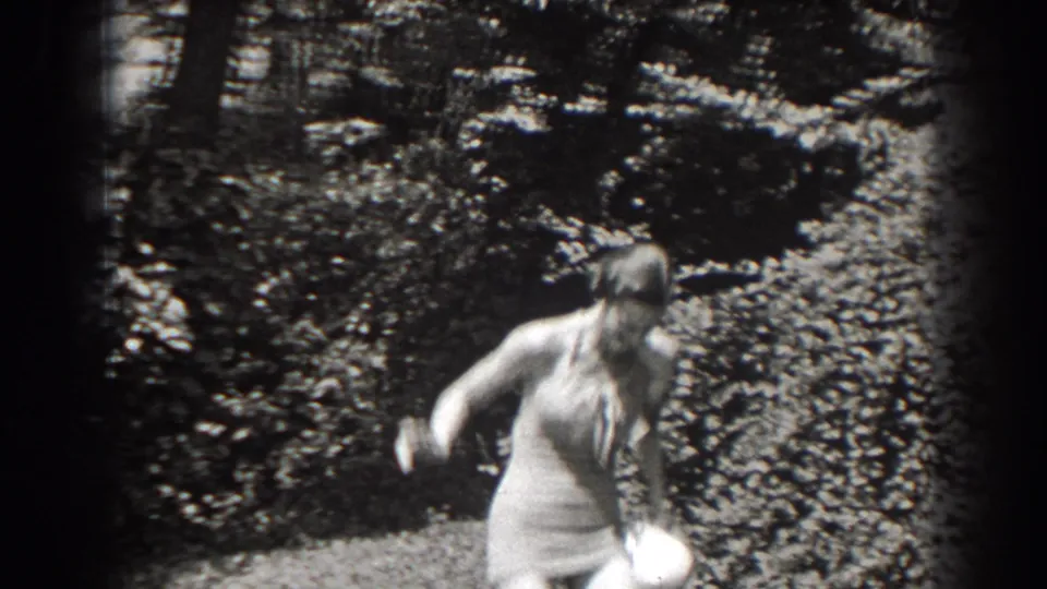 The woman shifts position in a wooded New Jersey setting, with her light swimsuit and hat visible against thick brush.