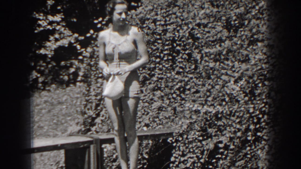 Woman in a one-piece bathing suit stands on a wooden deck holding a swim cap.