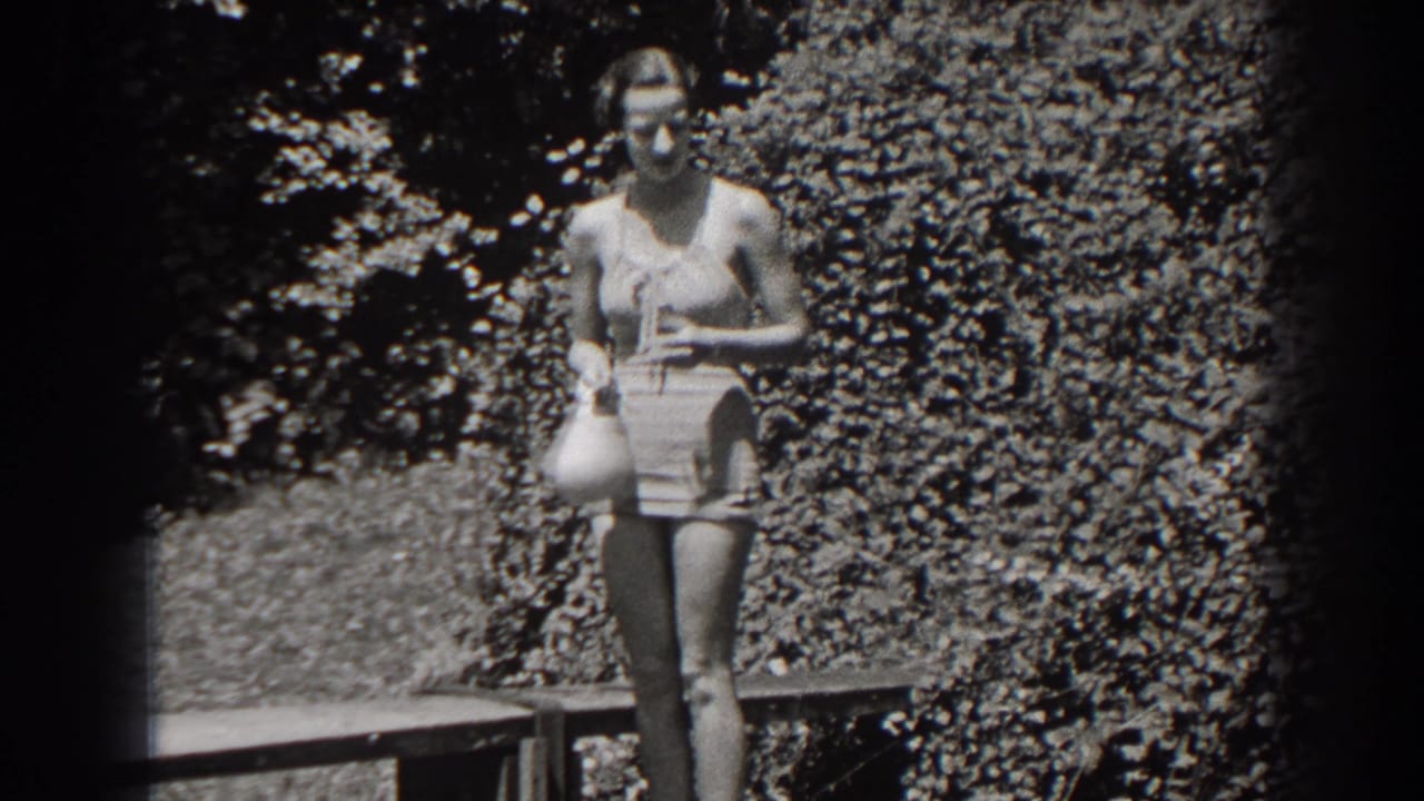 The woman remains posed in the New Jersey outdoor scene, holding a swim cap against a leafy background.