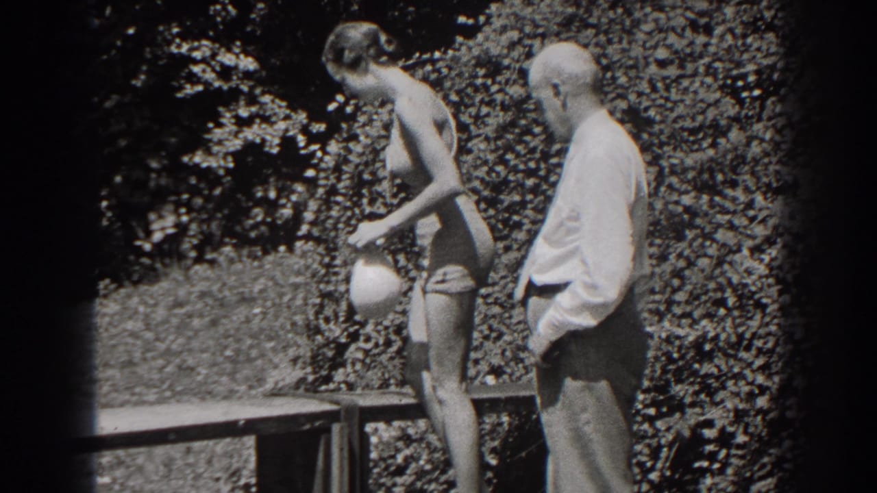 Woman in swimsuit faces away while holding a cap as a man stands nearby.