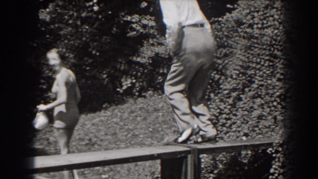 Woman in swimsuit holding a white cap while a man stands on a wooden platform nearby.