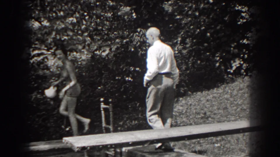 In the final frame, the woman walks away carrying a white cap as the older man stands on the wooden platform amid trees.