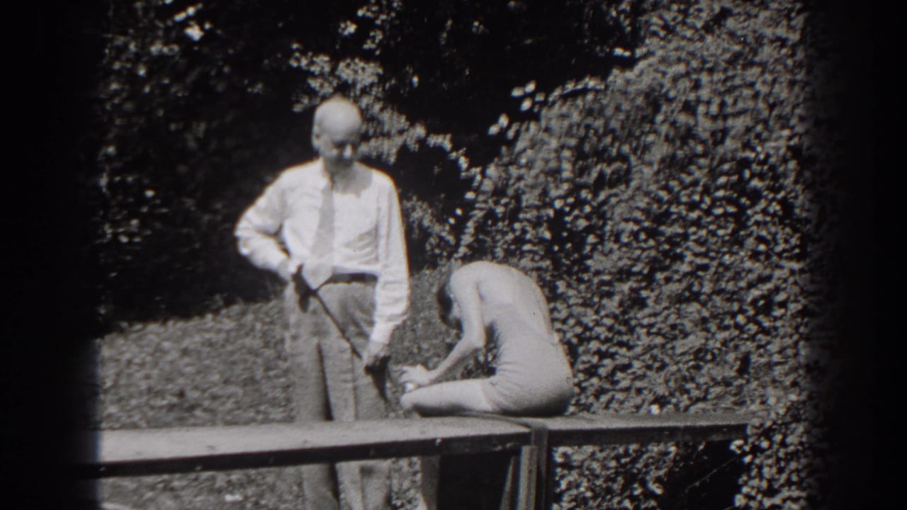 Man in a white shirt stands beside a seated woman on a wooden bench outdoors.