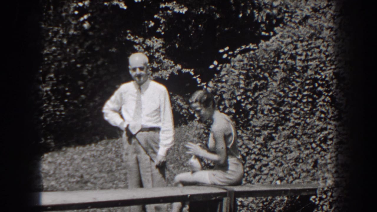 Man stands near the bench as the seated woman looks down and adjusts her swimsuit.