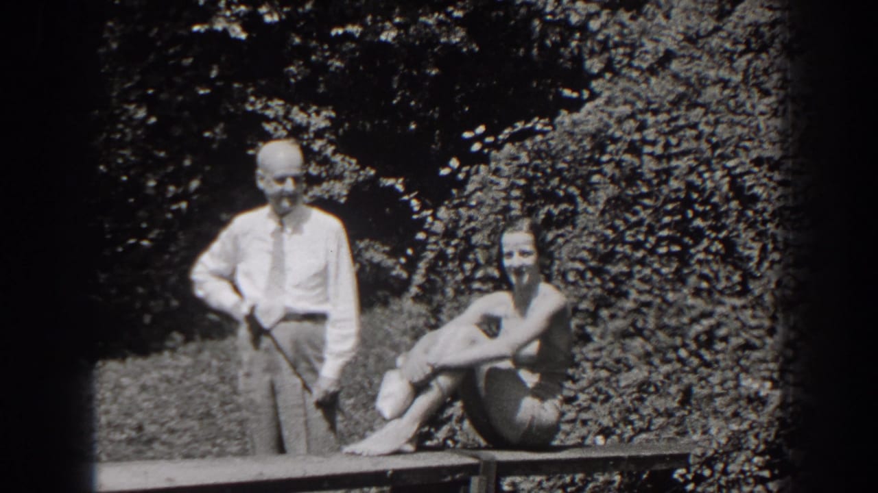 Man in shirt and tie stands beside a seated woman in a bathing suit outdoors.