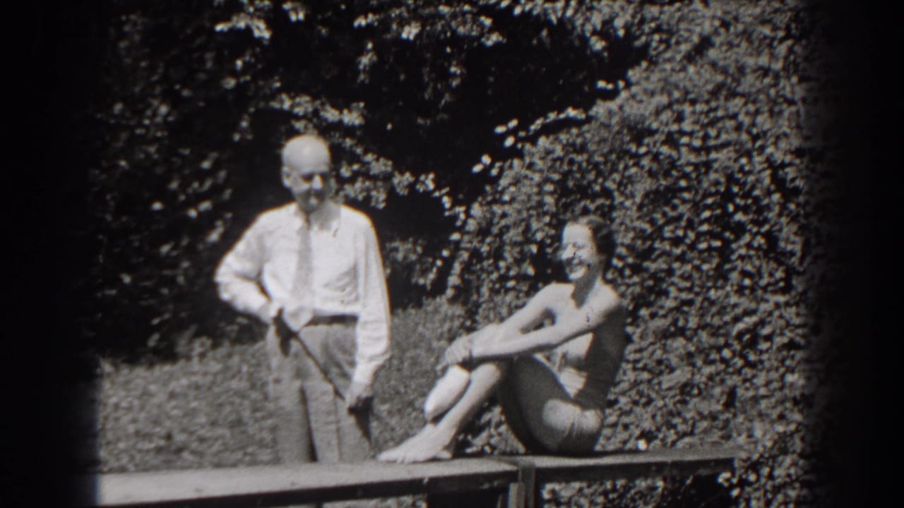 1938 New Jersey home-movie frame of a smiling seated woman in a bathing suit with a man standing beside her outdoors.