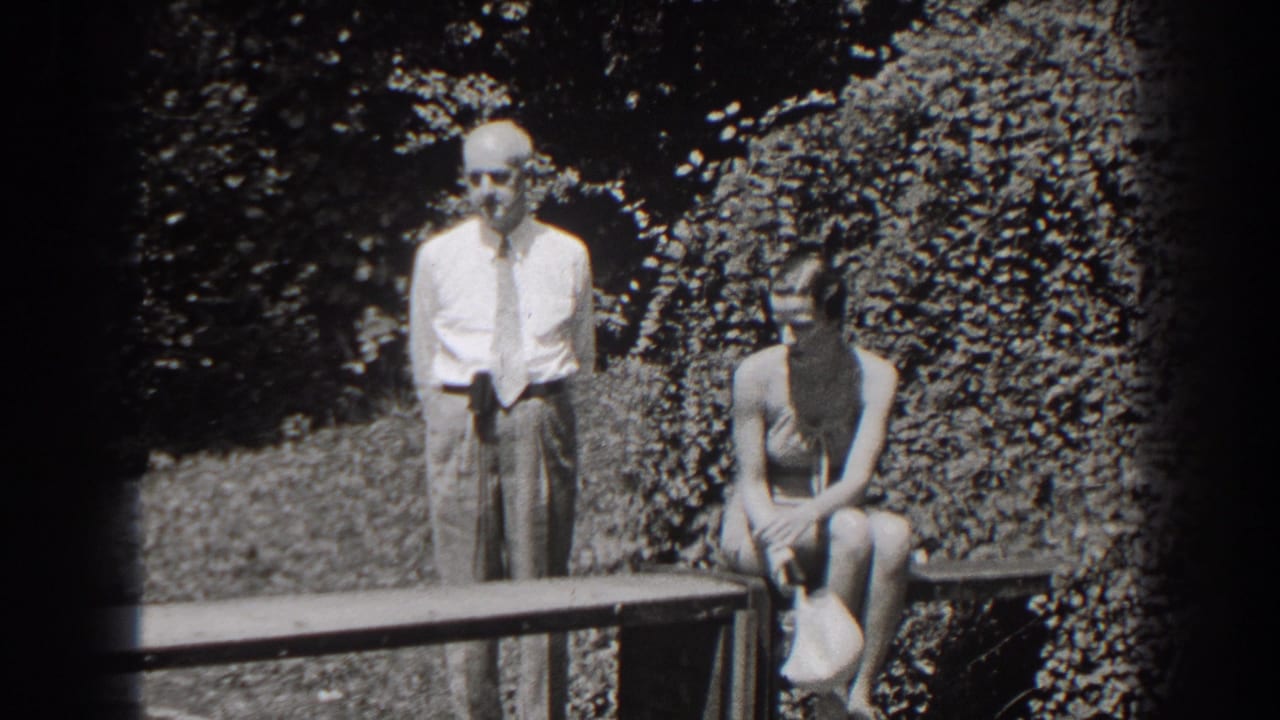 In the garden scene, the older man stands beside the bench while the seated woman holds a light-colored hat or object in her lap.
