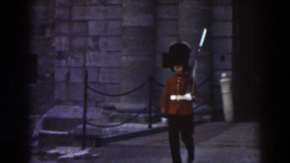 In 1938 Quebec footage, a ceremonial guard in a red tunic and tall black hat marches with a rifle near stone buildings.