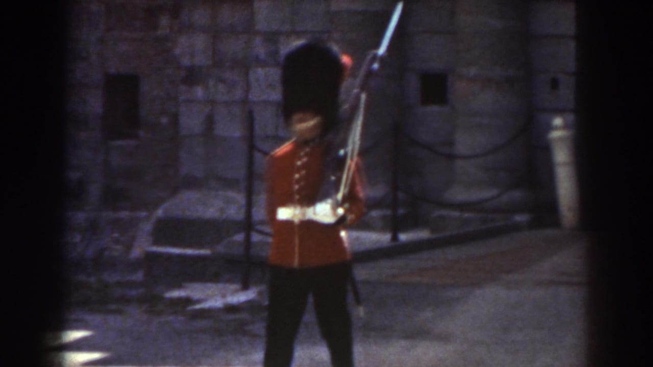 Uniformed guard in red coat carries a rifle while passing stone walls.