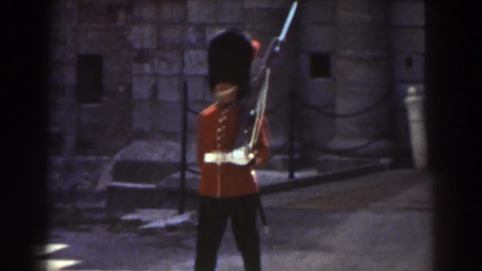 A red-coated ceremonial guard carrying a rifle moves across the frame in the supported 1938 Quebec setting.