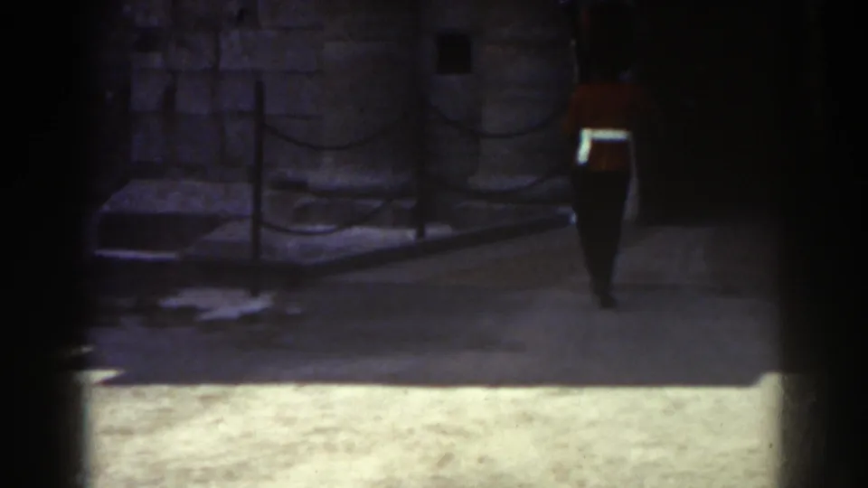 In 1938 Quebec footage, a red-uniformed sentry stands at attention near a rope barrier and stone fortress wall.